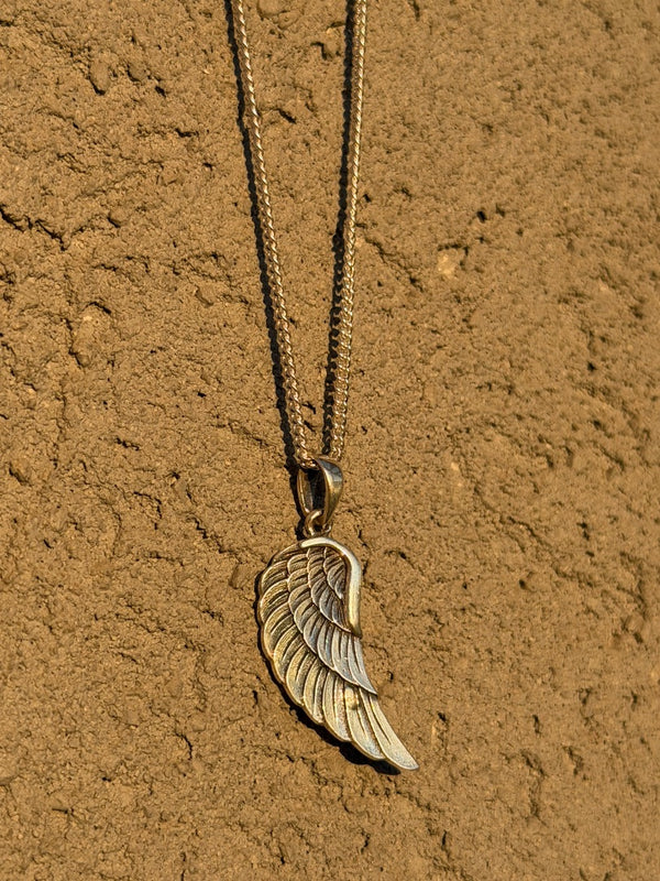 Gold wing-shaped pendant necklace on a textured brown surface