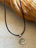 Gold elephant pendant necklace on a black cord against a wooden background