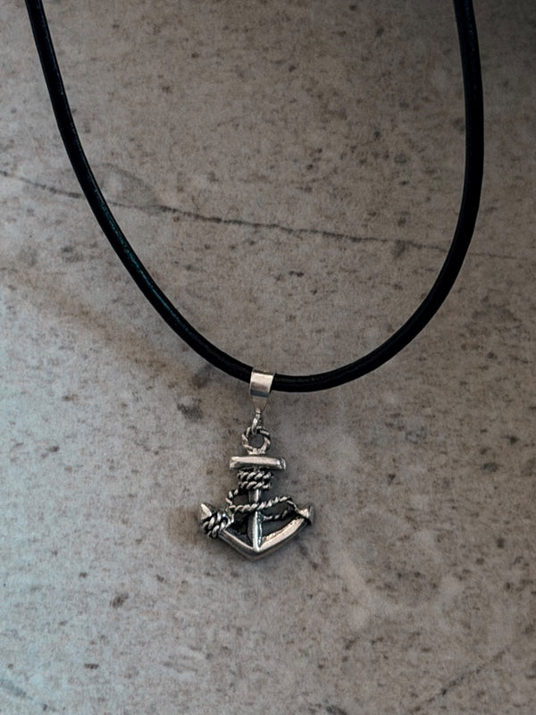 Silver anchor pendant on a black cord against a gray background