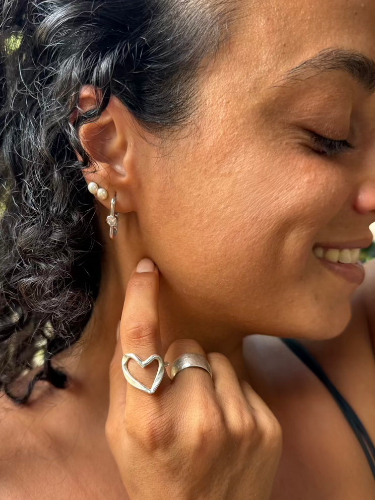 Close-up of a woman wearing silver hoop earrings and a heart-shaped ring.