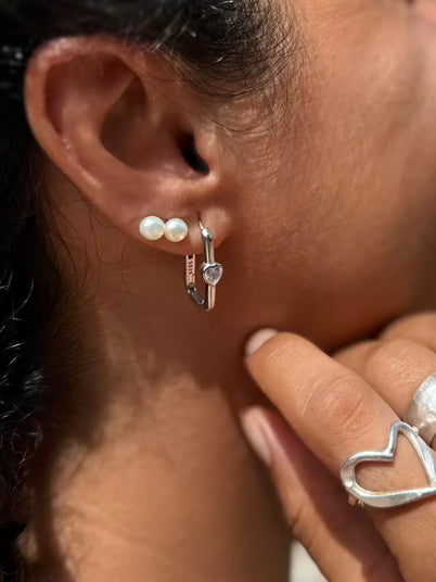 Close-up of an ear with pearl earrings and a silver ring.