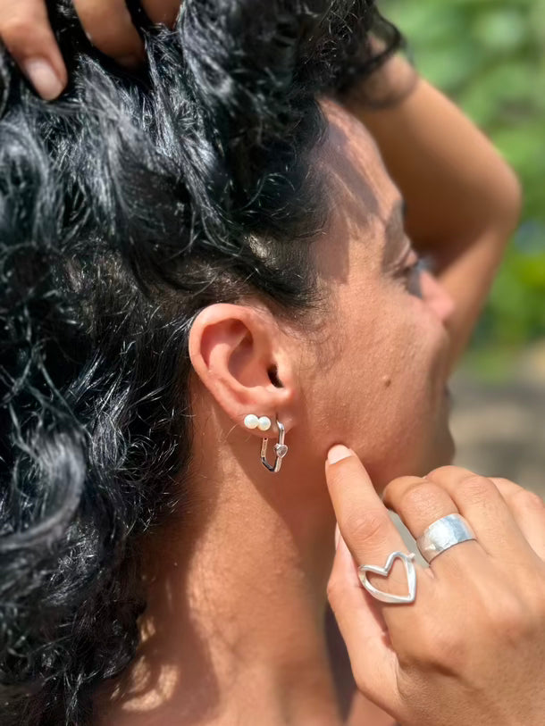 Person with silver earrings and ring touching their hair outdoors