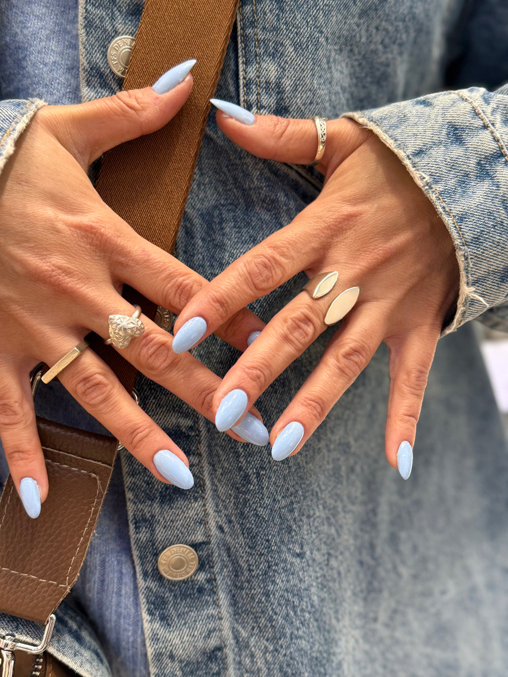 Close-up of hands with light blue nail polish wearing rings on a denim background