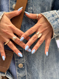 Close-up of hands with light blue nail polish wearing rings on a denim background
