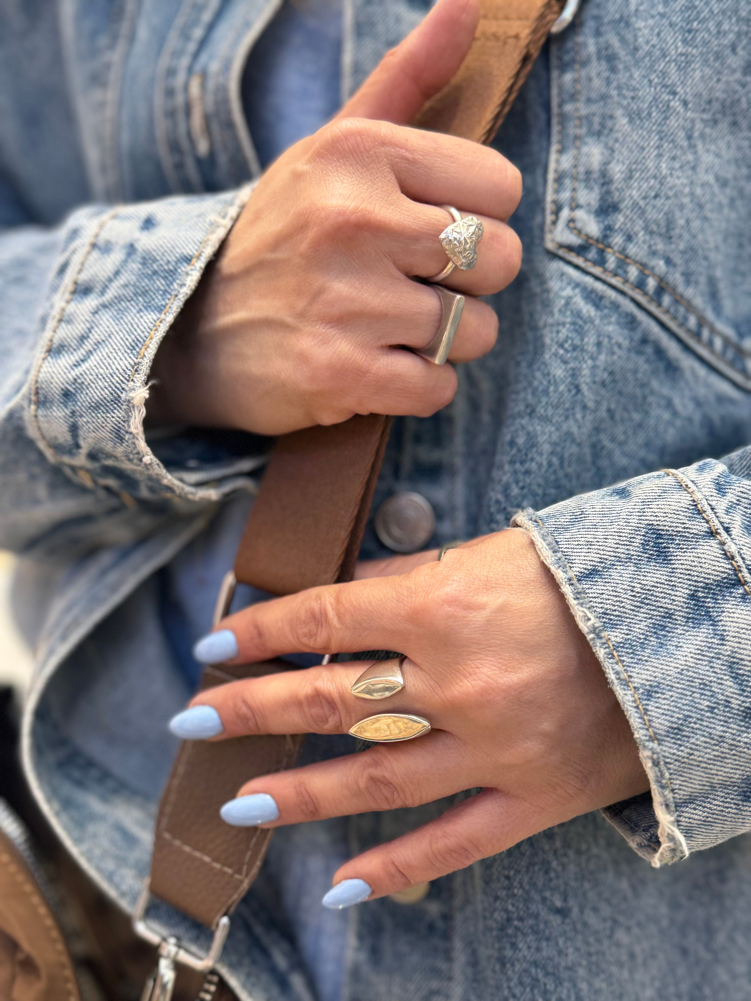 Close-up of hands wearing multiple rings with a denim jacket background