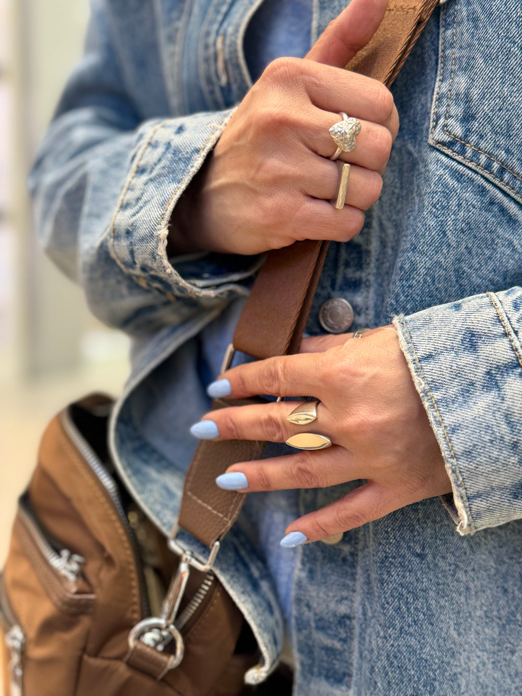 Close-up of hands wearing rings with a denim jacket and brown bag.