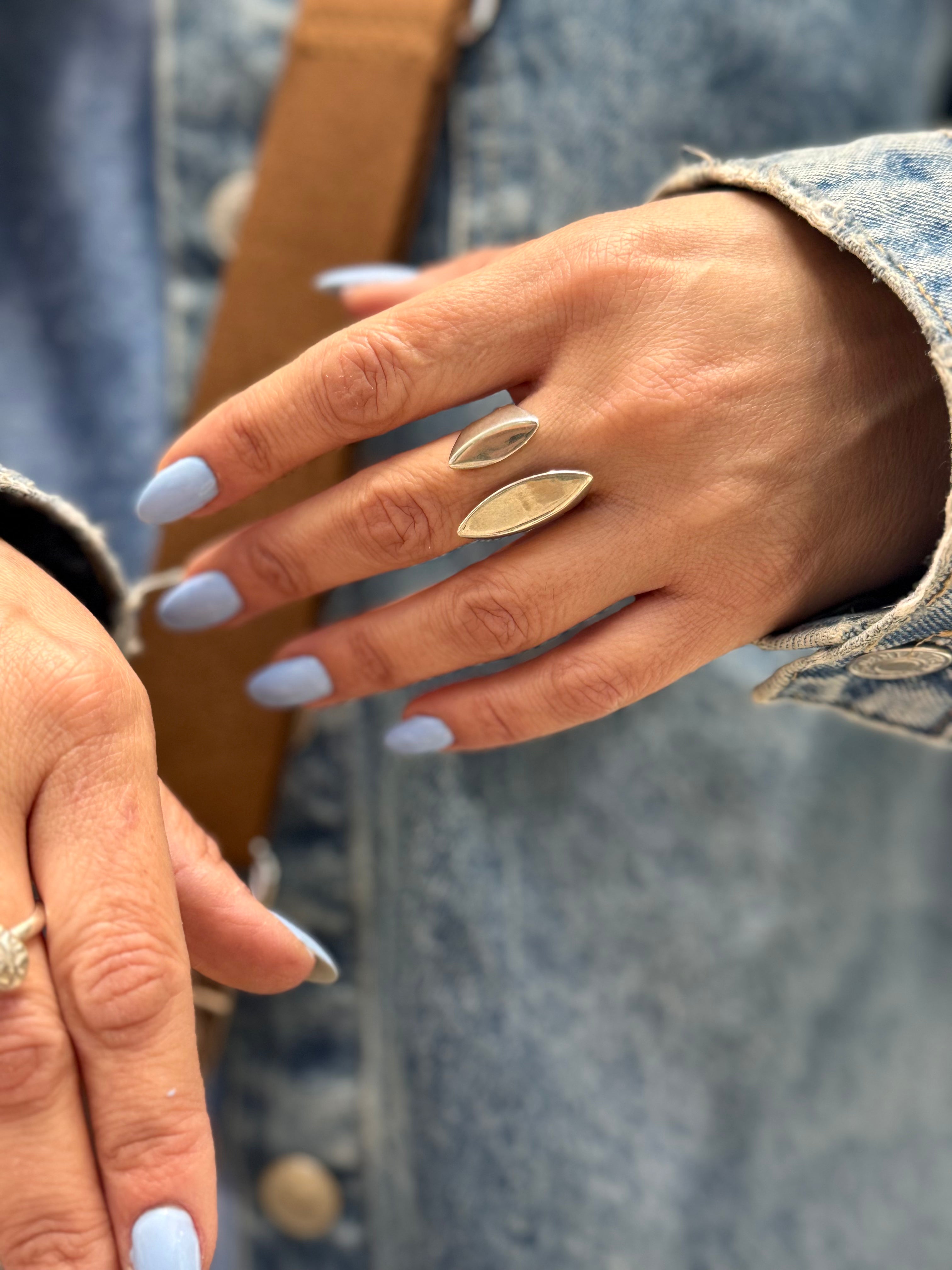 Close-up of a hand with silver rings and light blue nail polish, wearing a denim jacket.
