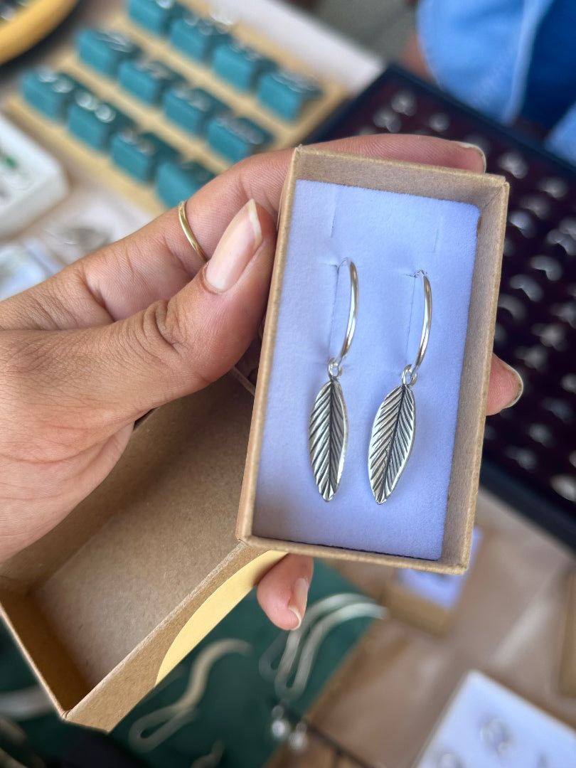 Hand holding a box with silver feather earrings inside, keyboard in the background
