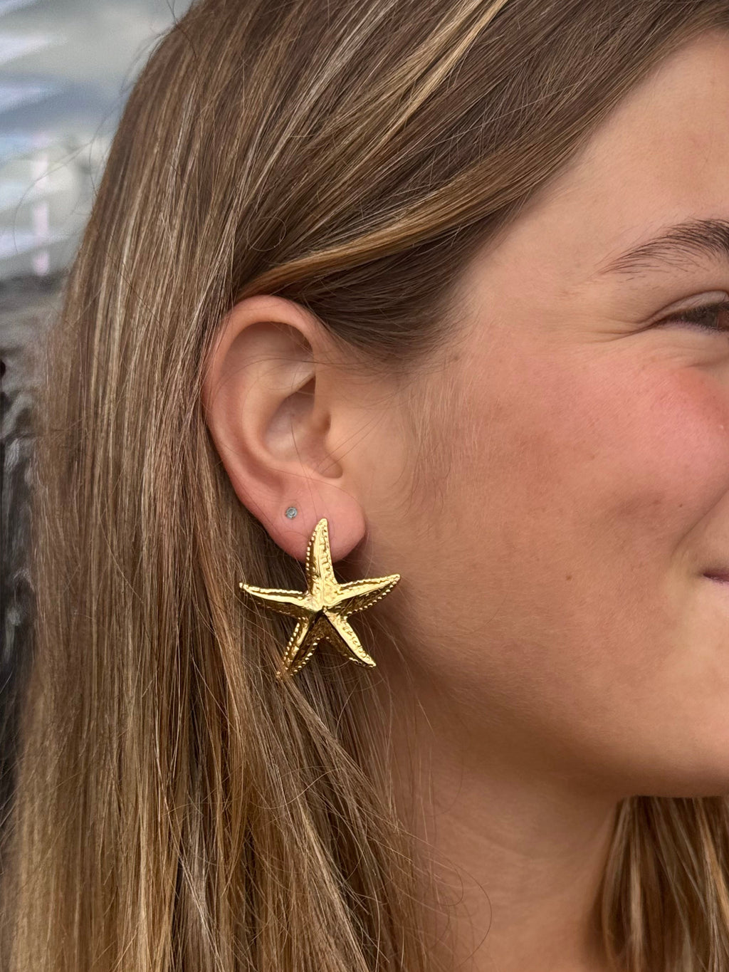 Woman wearing a gold starfish earring with a blurred indoor background