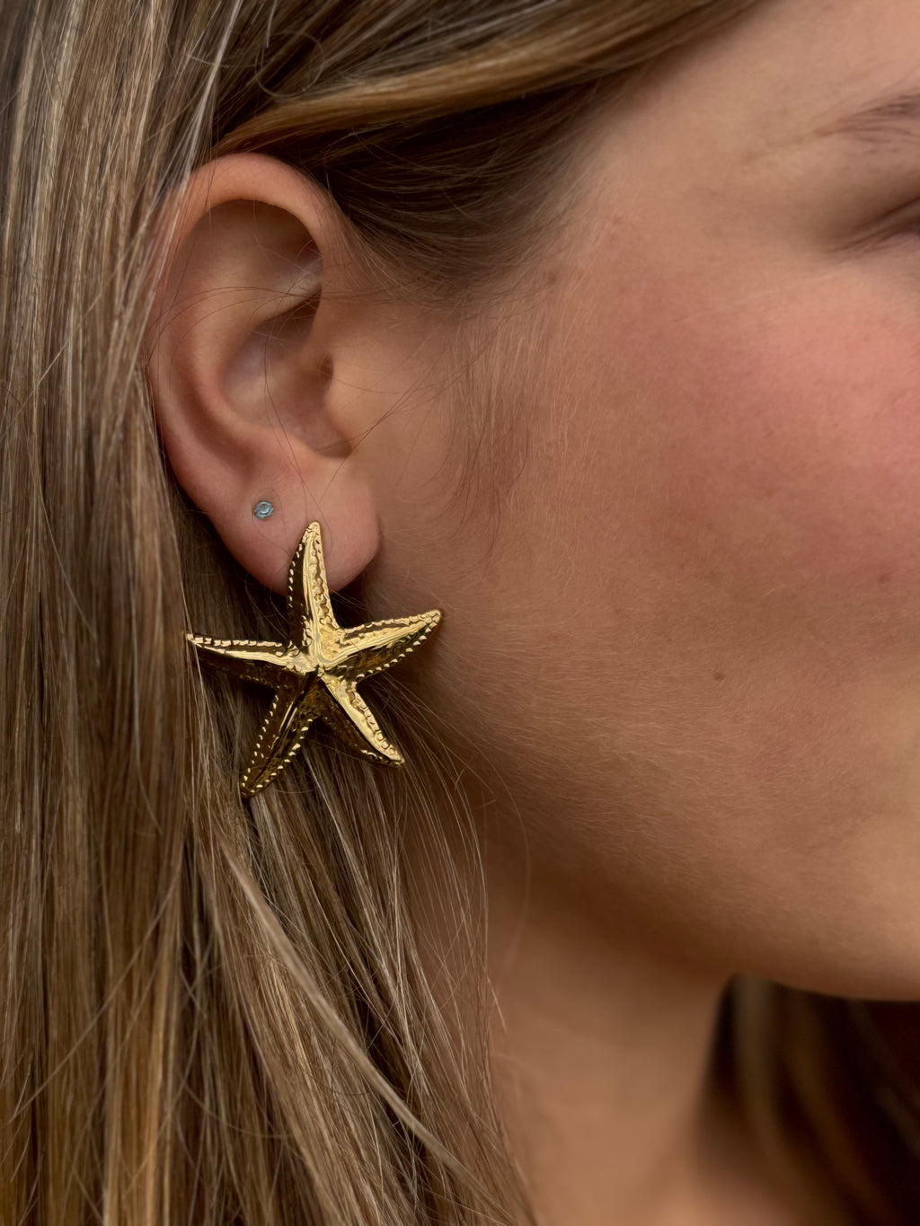 Close-up of a person wearing a gold starfish earring.