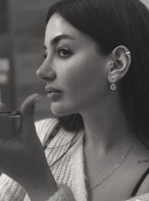 Black and white photo of a woman holding a cup, wearing earrings and a necklace.