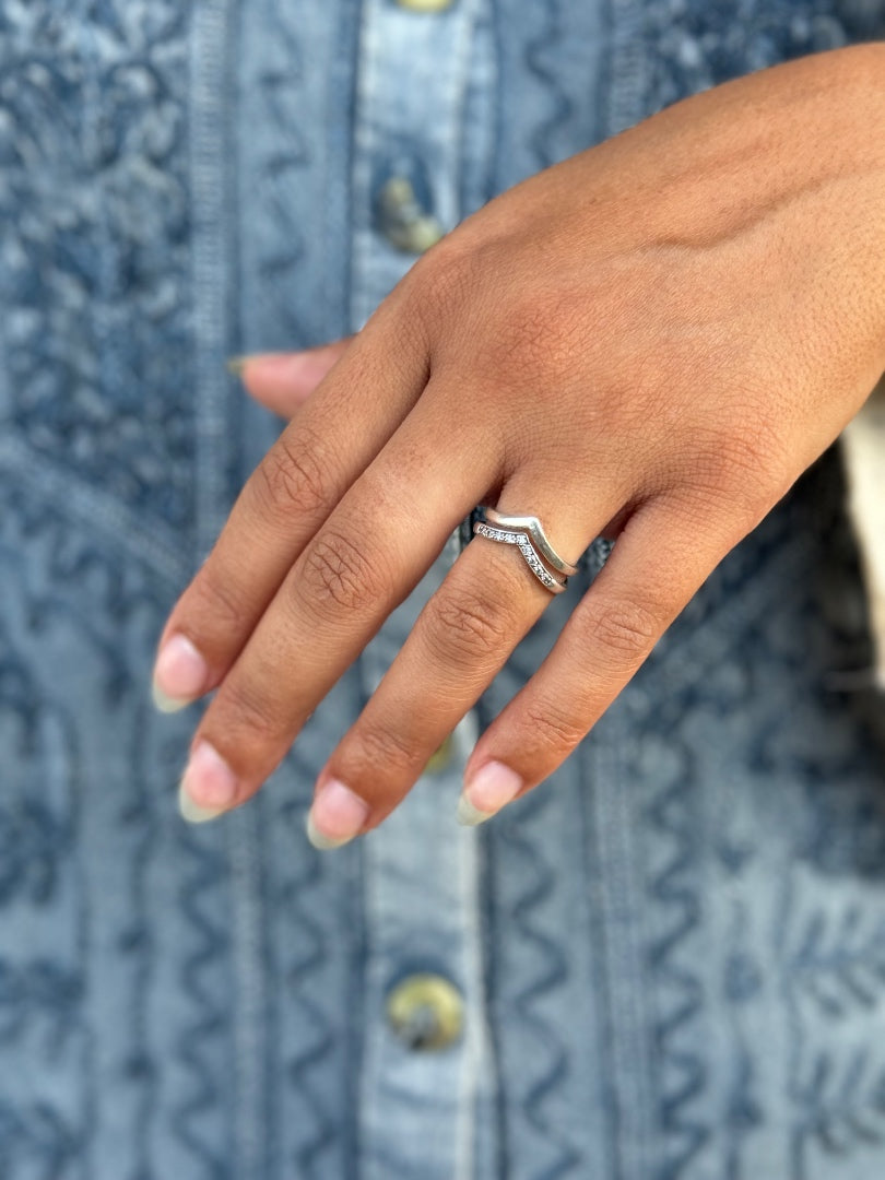 A close-up of a person's hand wearing a silver chevron ring with small clear stones, set against a blue patterned denim shirt.