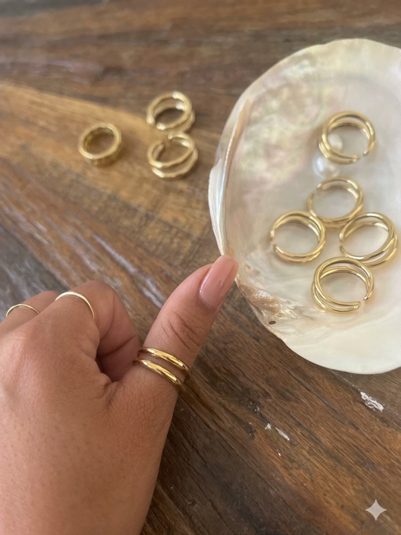 Gold rings on a wooden surface with a hand wearing a gold ring.