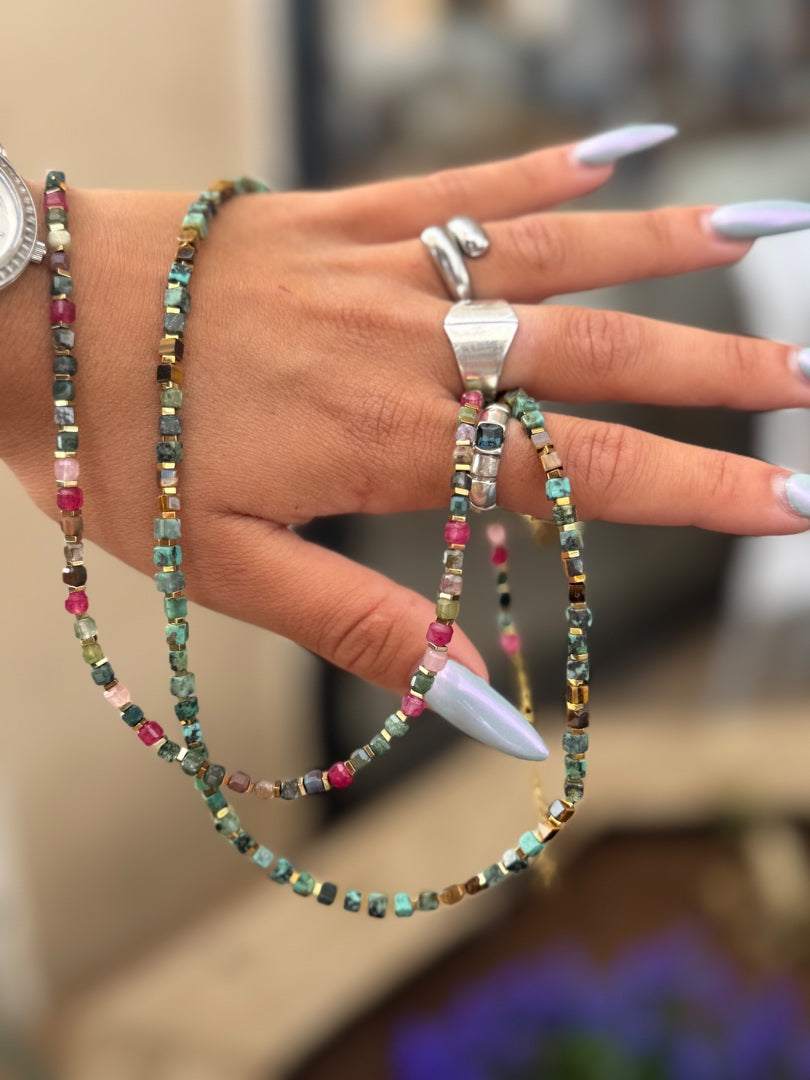 Hand wearing multiple beaded bracelets and rings with a blurred background