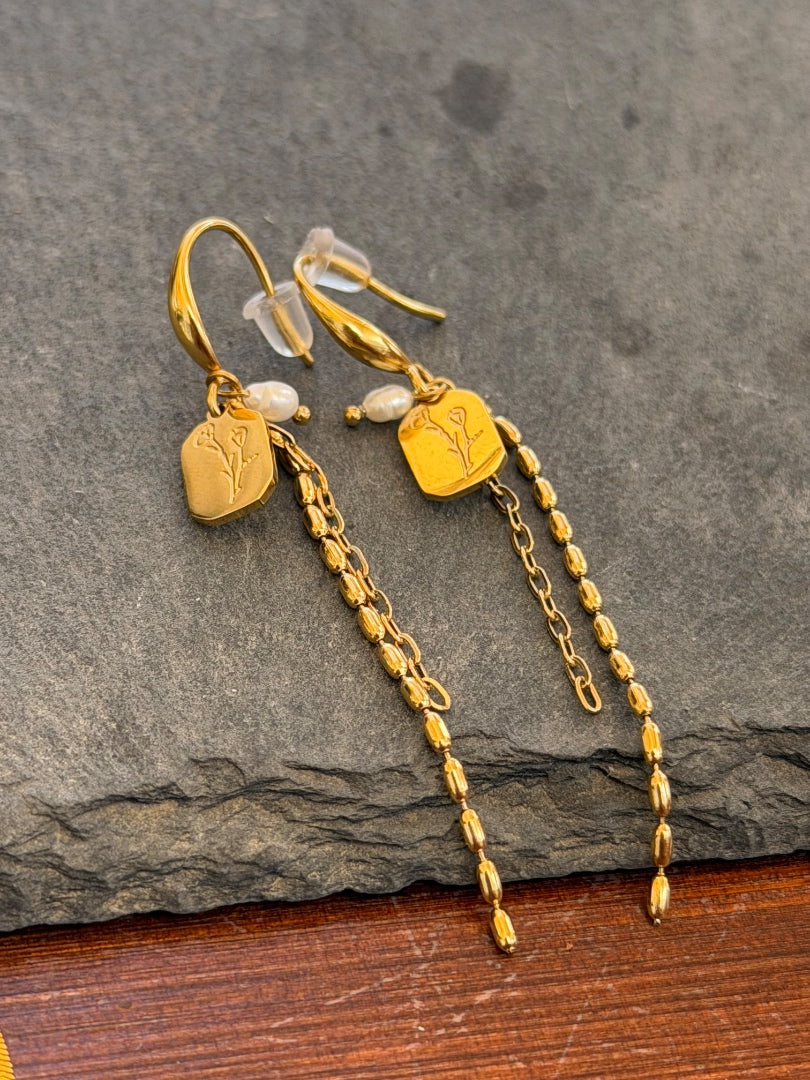 Gold earrings with chain drops on a stone surface