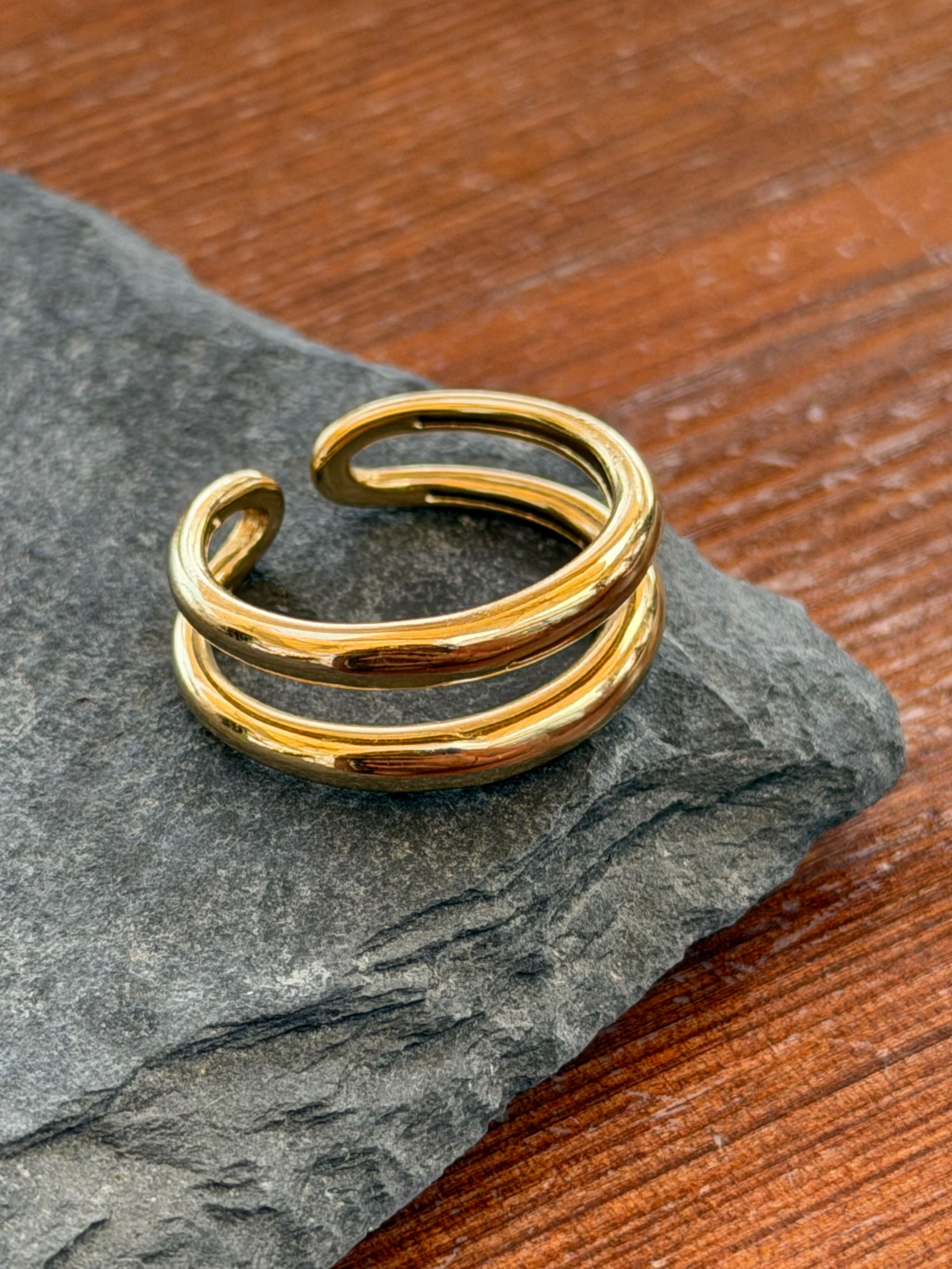 Gold ring with three bands on a dark stone surface