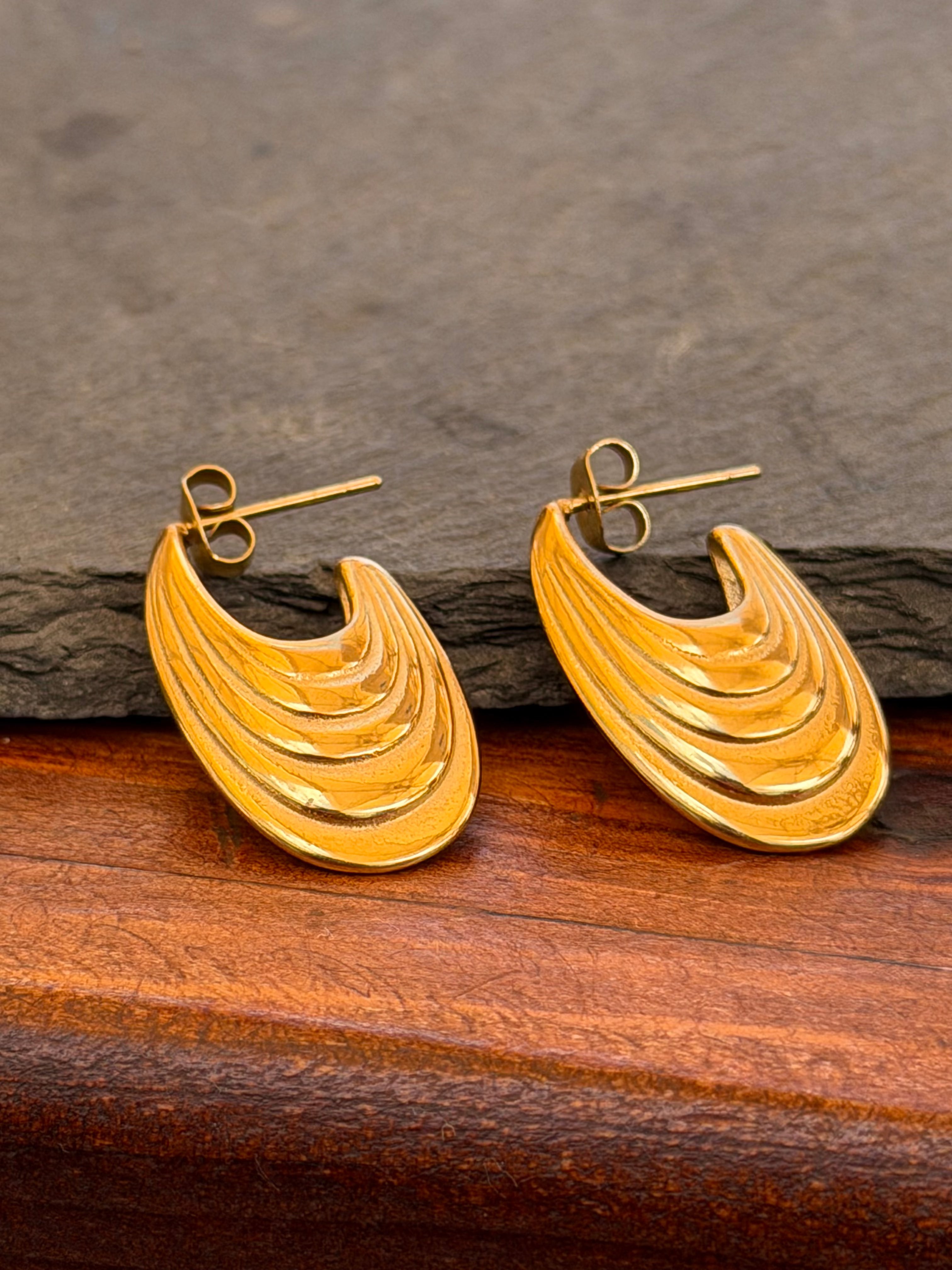 Gold earrings on a wooden surface with a stone background