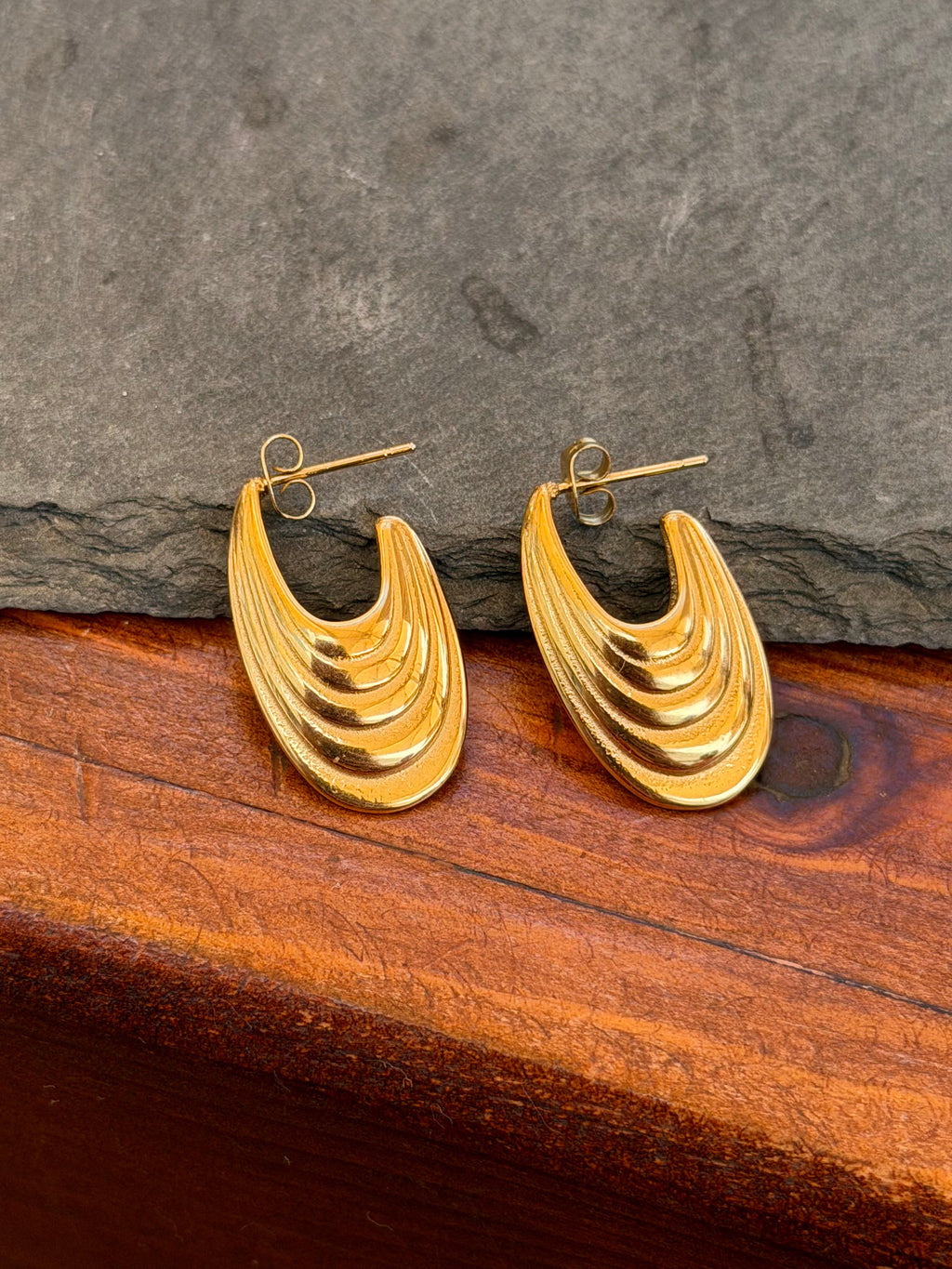 Gold hoop earrings on a stone surface