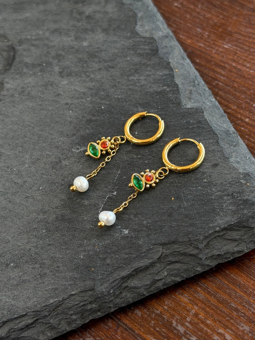 Gold hoop earrings with pearl and gemstone accents on a dark stone surface
