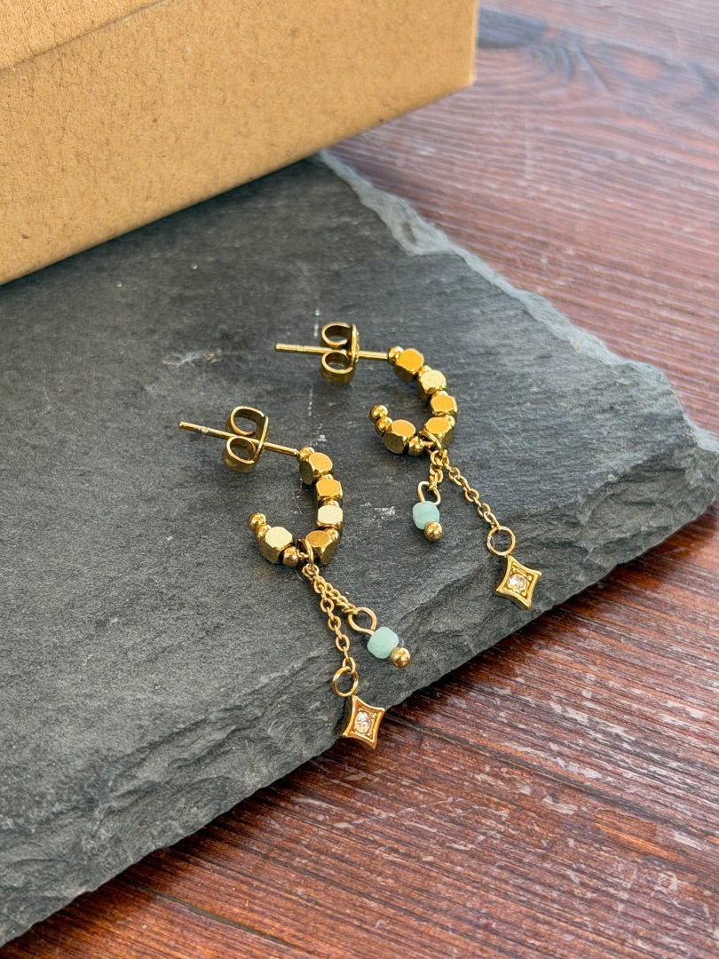 Gold hoop earrings with small beads on a dark stone surface