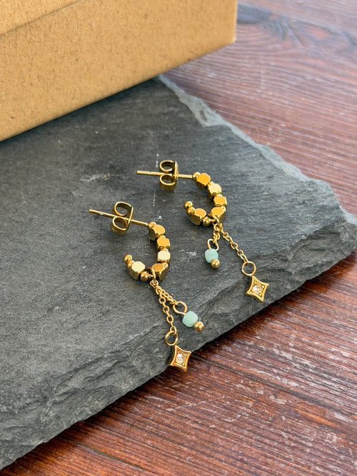 Gold hoop earrings with small beads on a dark stone surface