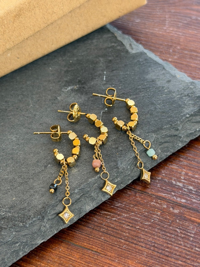 Gold earrings with small charms on a dark stone surface