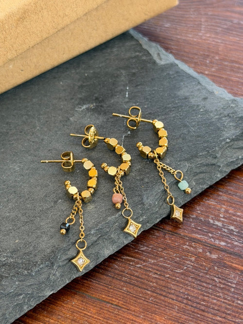 Gold earrings with small charms on a dark stone surface