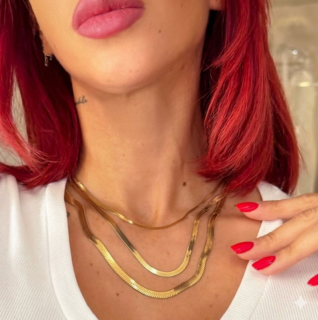 Close-up of a person with red hair wearing a gold necklace, with a blurred background.