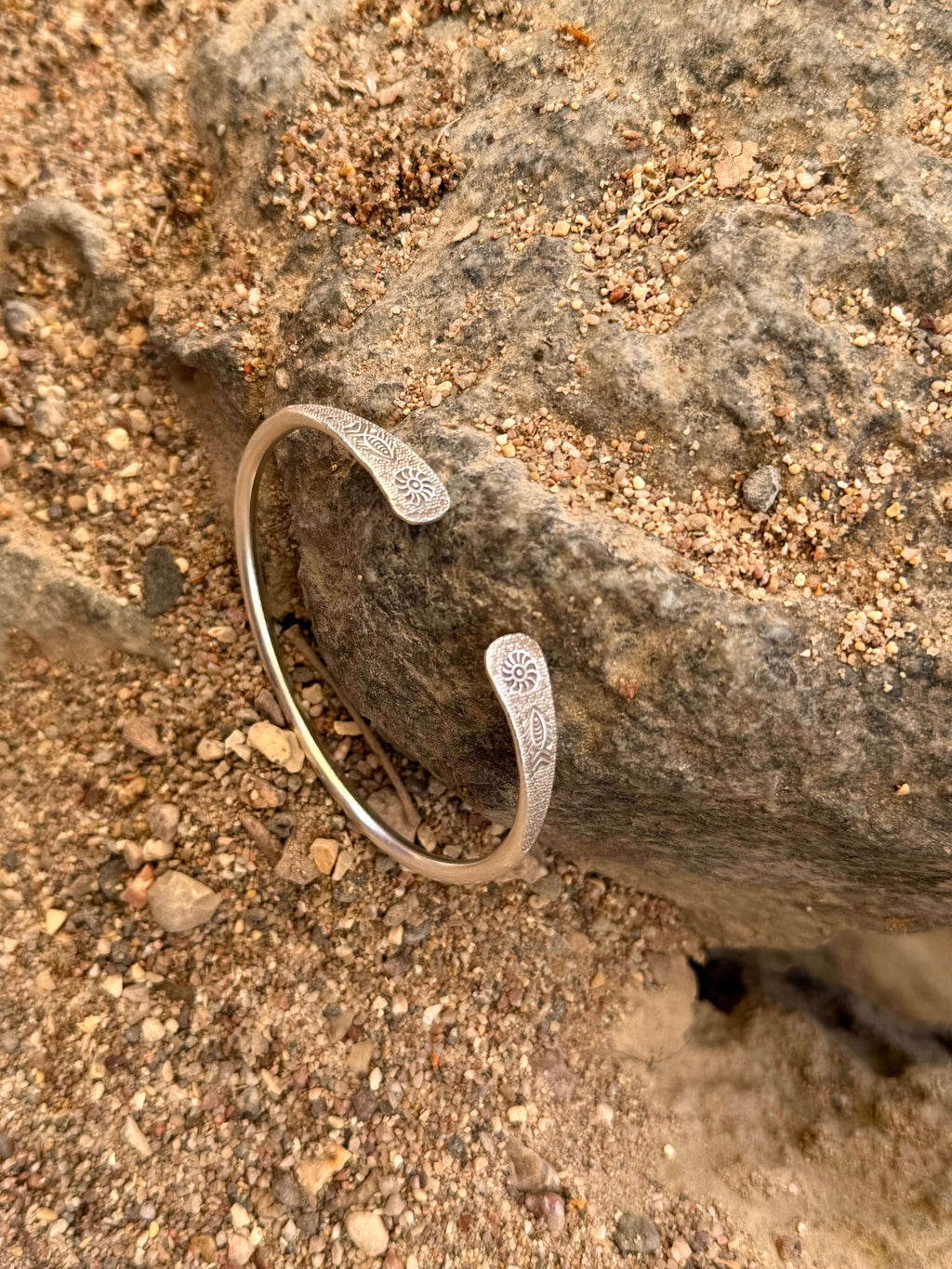 Silver bracelet on a sandy surface with rocks