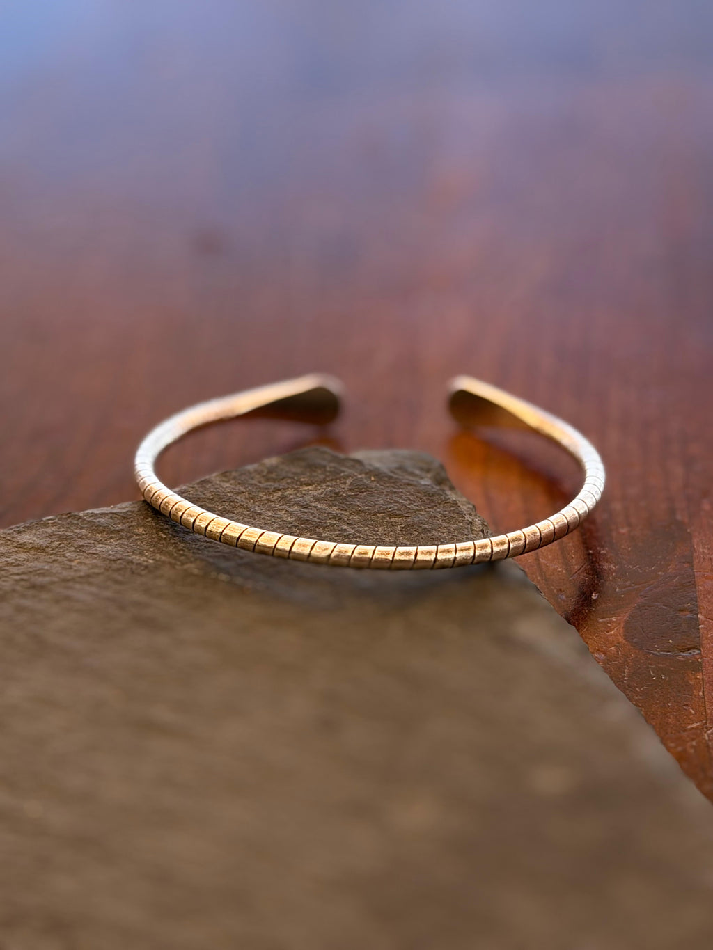 Gold bracelet on a stone surface with a blurred natural background