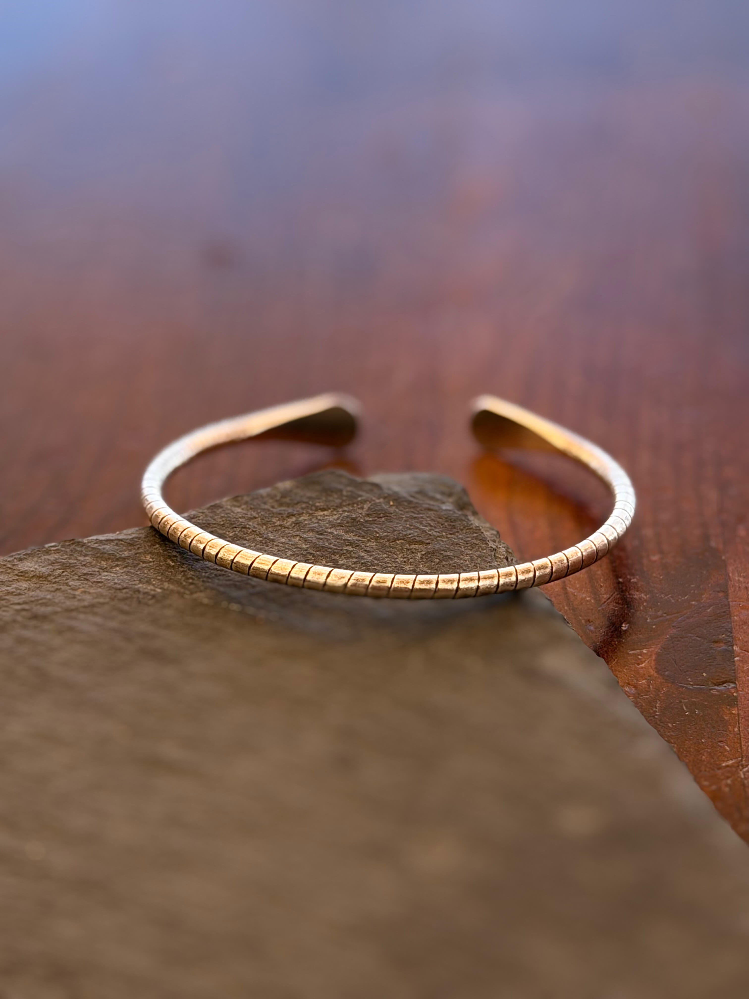 Gold bracelet on a stone surface with a blurred natural background