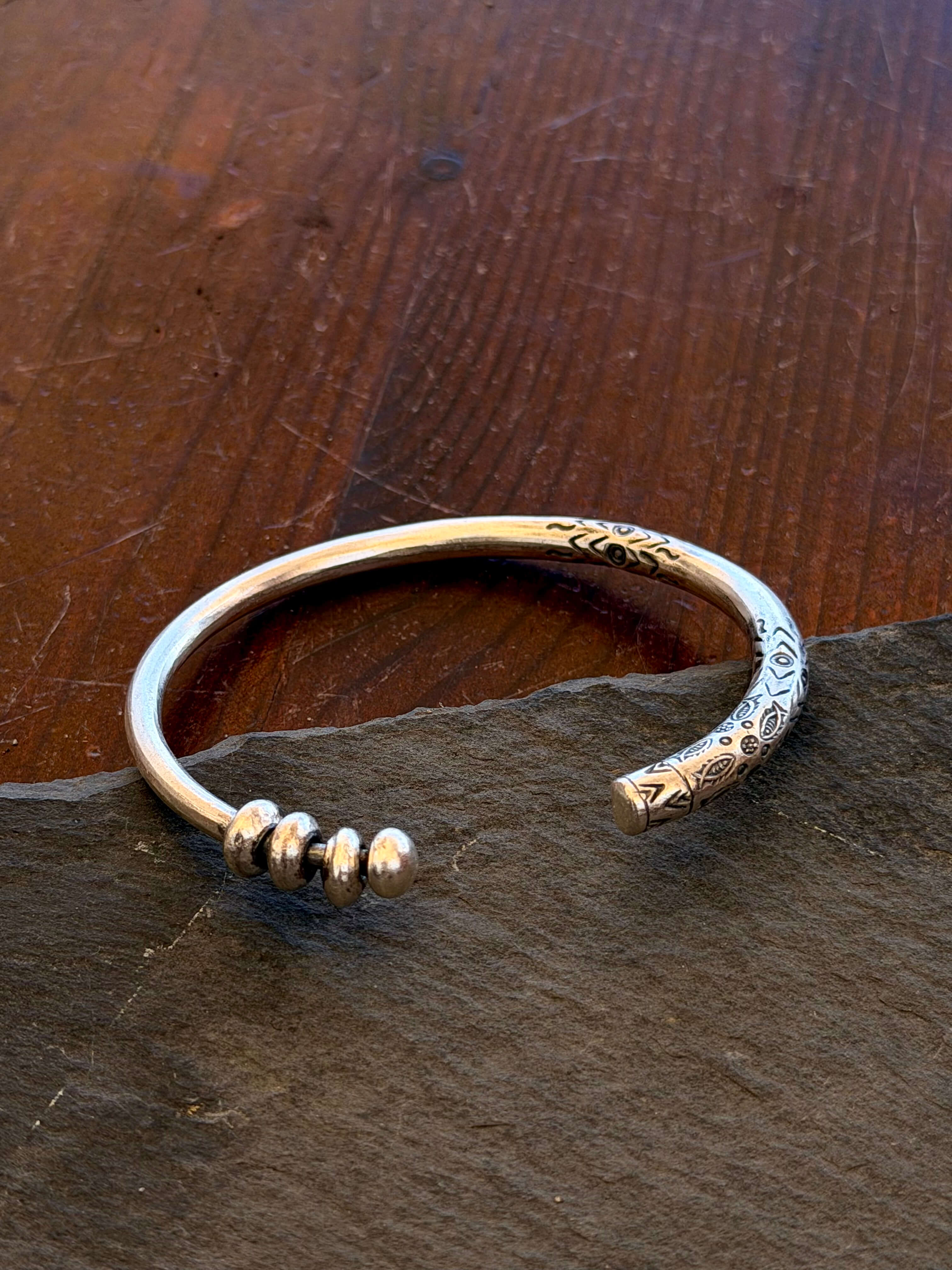 Silver bracelet with intricate designs on a dark stone surface