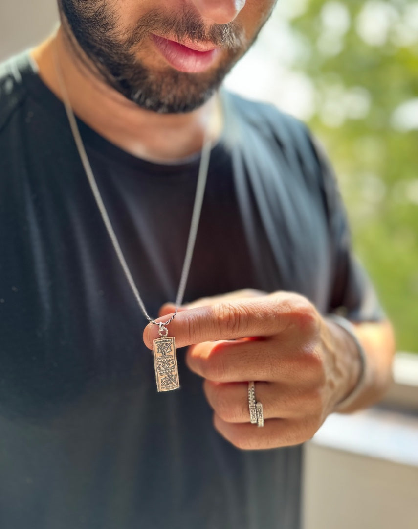 Man holding a necklace with a pendant, wearing a dark shirt outdoors.