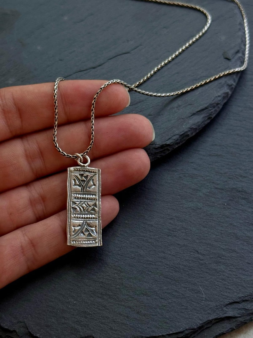 Silver pendant necklace held by a hand on a dark surface