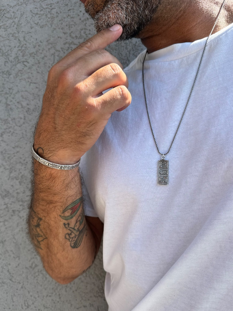 Person wearing a white t-shirt with a necklace and bracelet, standing against a neutral background.
