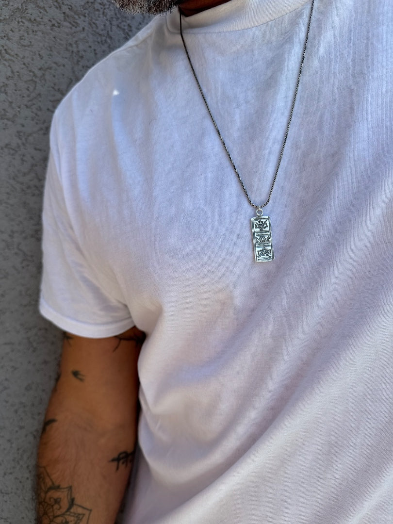 Person wearing a white t-shirt with a necklace featuring a rectangular pendant.