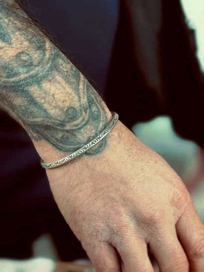 Close-up of a hand with a silver bracelet and tattoo on a blurred background
