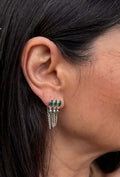Close-up of an ear wearing a set of earrings with green gemstones.