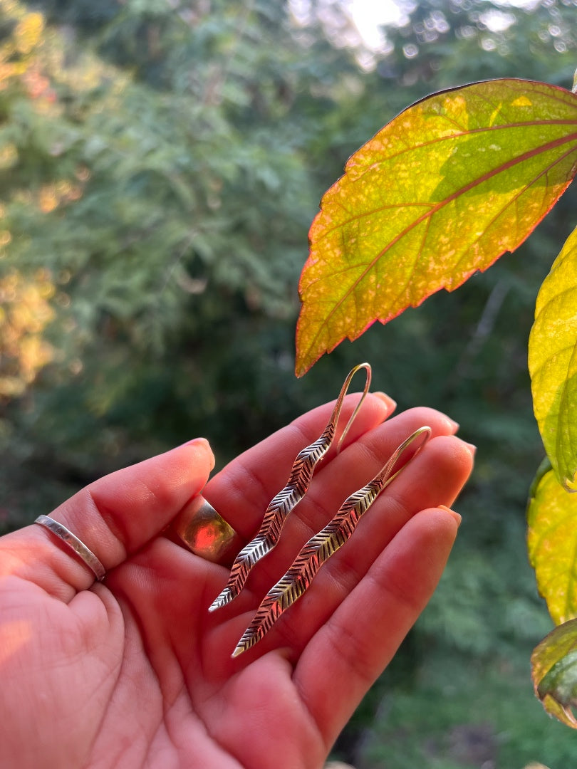 Hand holding three decorative earrings with a natural leafy background