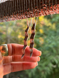Hand holding a pair of unique earrings with a blurred natural background
