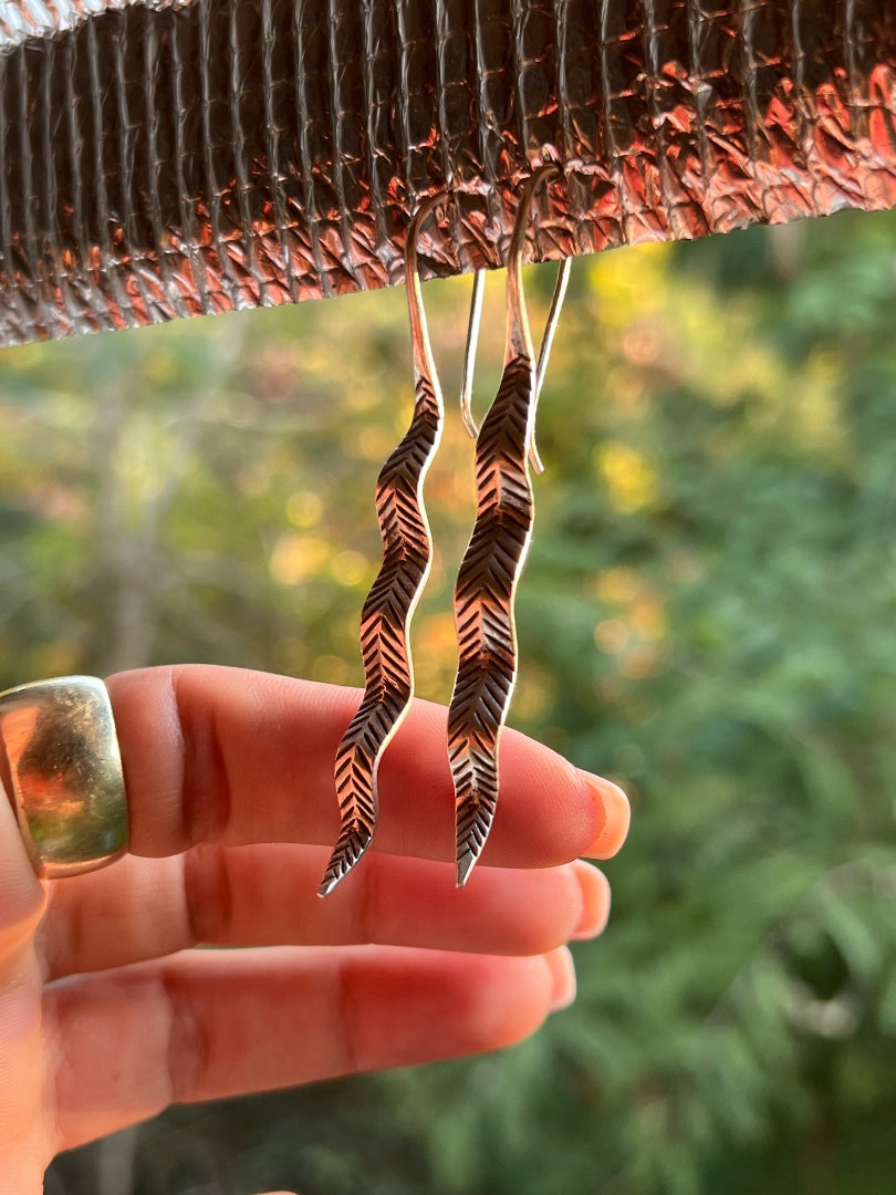 Hand holding a pair of unique earrings with a blurred natural background