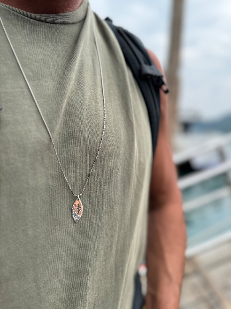 Person wearing a necklace with a pendant, standing outdoors.