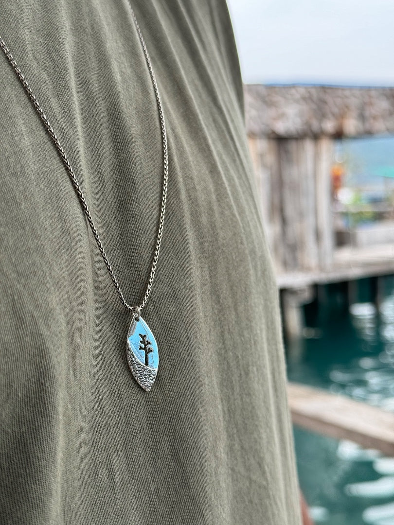 Necklace with a pendant on a person wearing a green shirt by a waterfront.
