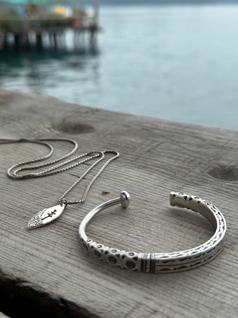 Silver necklace and bracelet on a wooden surface with a blurred water background