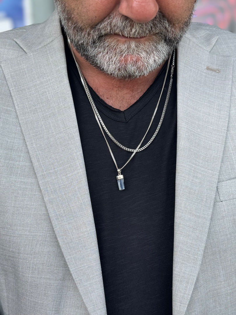 Man wearing a gray suit jacket and black shirt with layered necklaces.