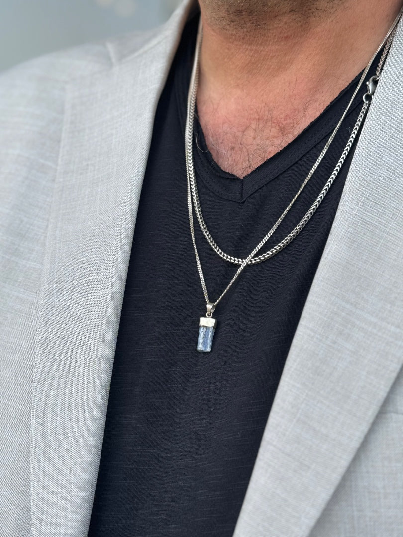 Person wearing a necklace with a pendant, dressed in a gray blazer and black shirt.