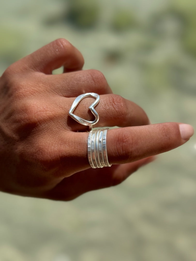 Hand wearing a silver heart-shaped ring with a blurred natural background