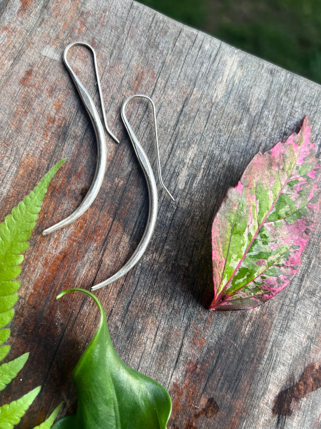 Silver earrings on a wooden surface with leaves