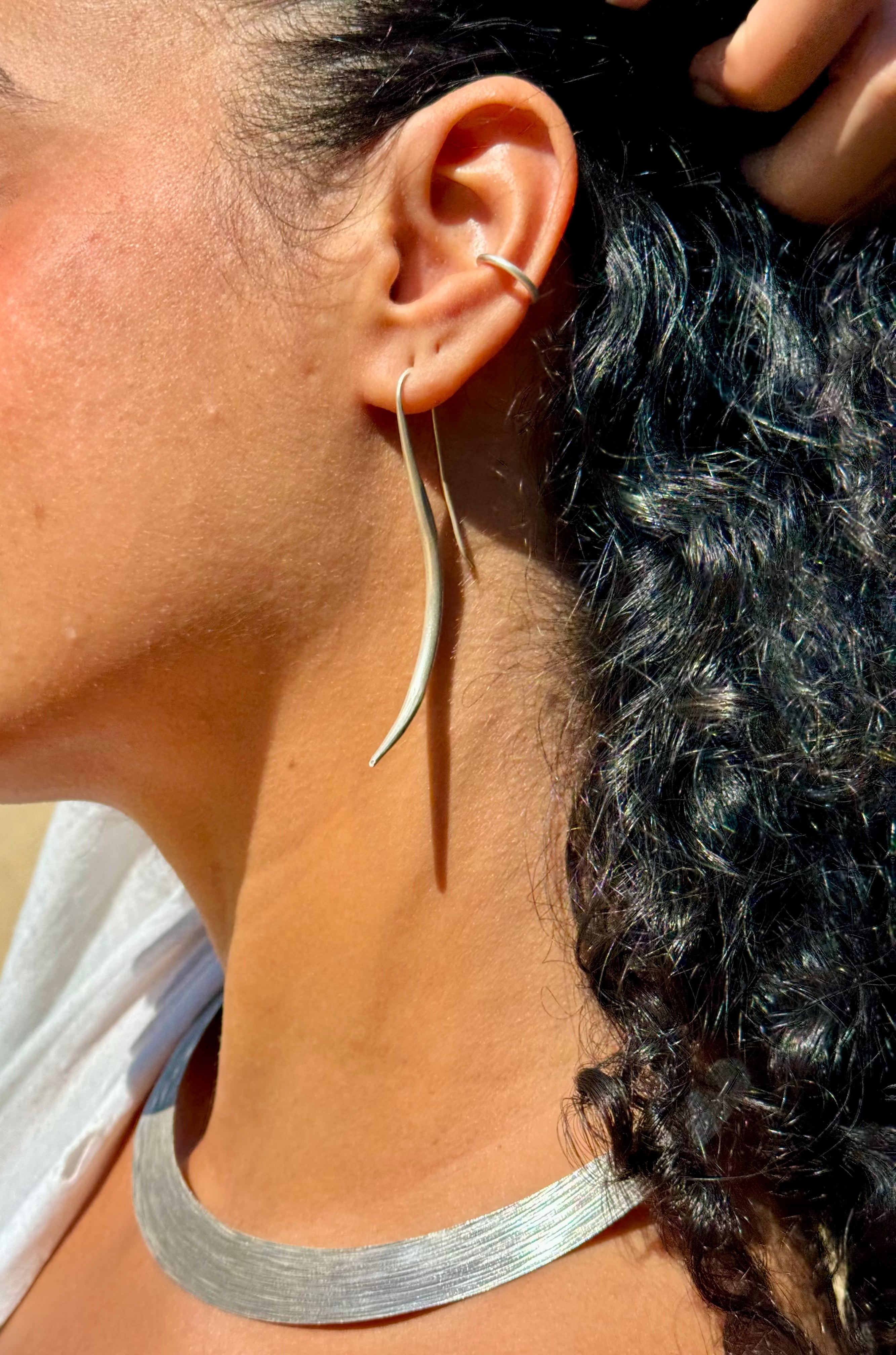 Close-up of a person wearing silver hoop earrings and a necklace.