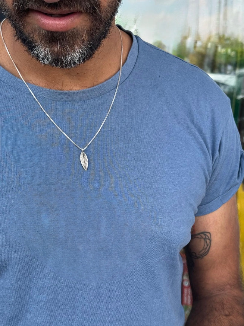 Man wearing a blue t-shirt and a necklace with a leaf pendant.